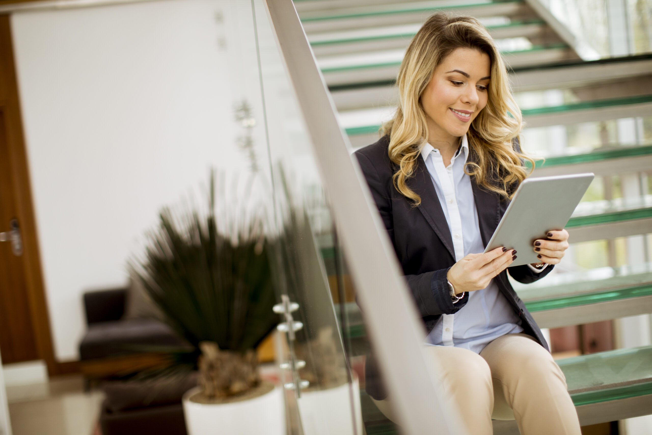 Freundliche junge Geschäftsfrau sitzt mit einem Tablet auf einer Treppe in einem modernen Büro